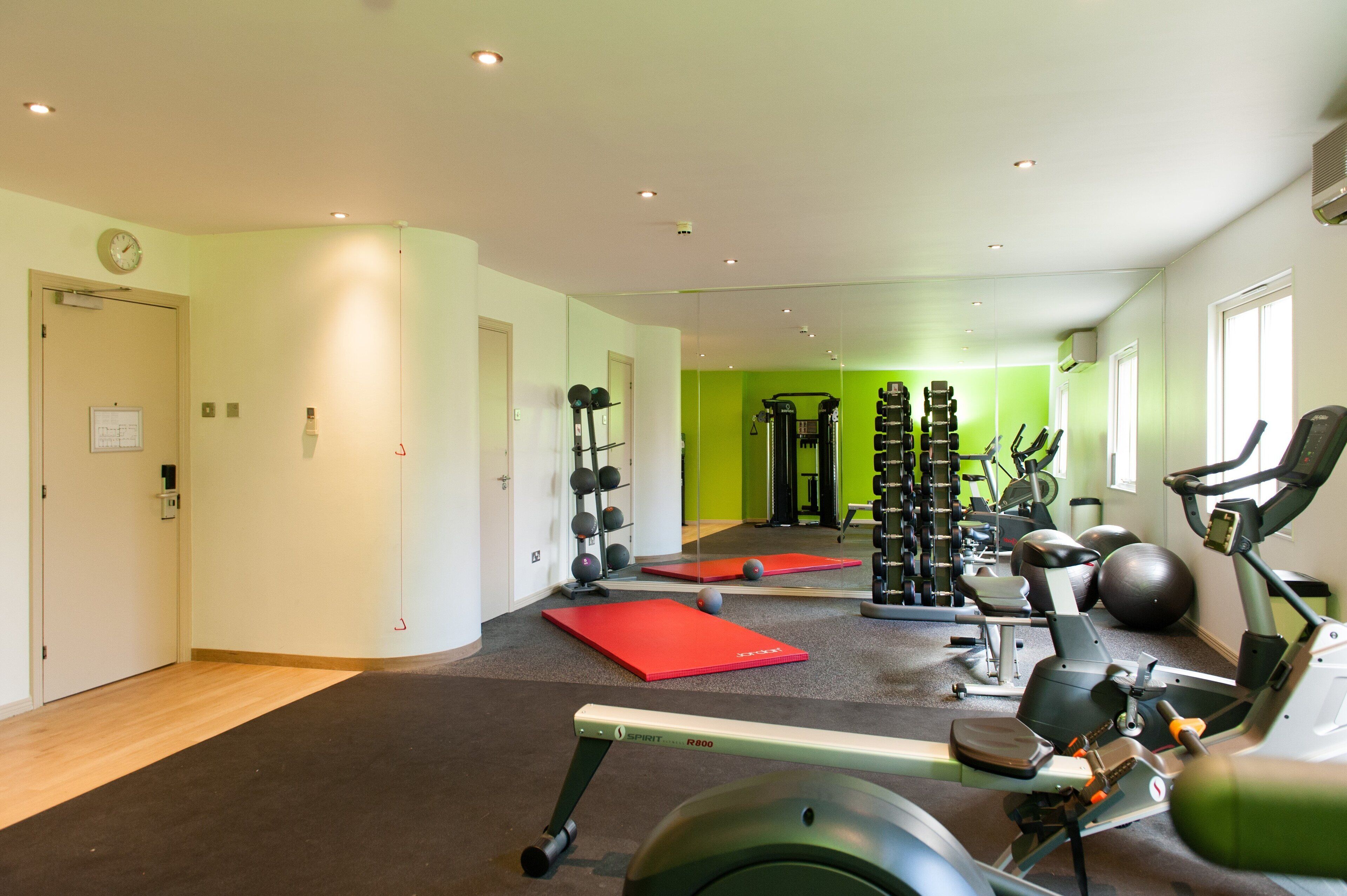 Ein Fitnessstudio mit Cardiogeräten, Kraftstationen und roten Trainingsmatten.
