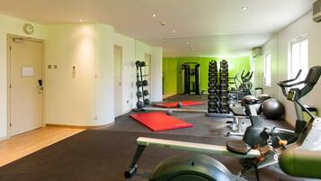 Ein Fitnessstudio mit Cardiogeräten, Kraftstationen und roten Trainingsmatten.