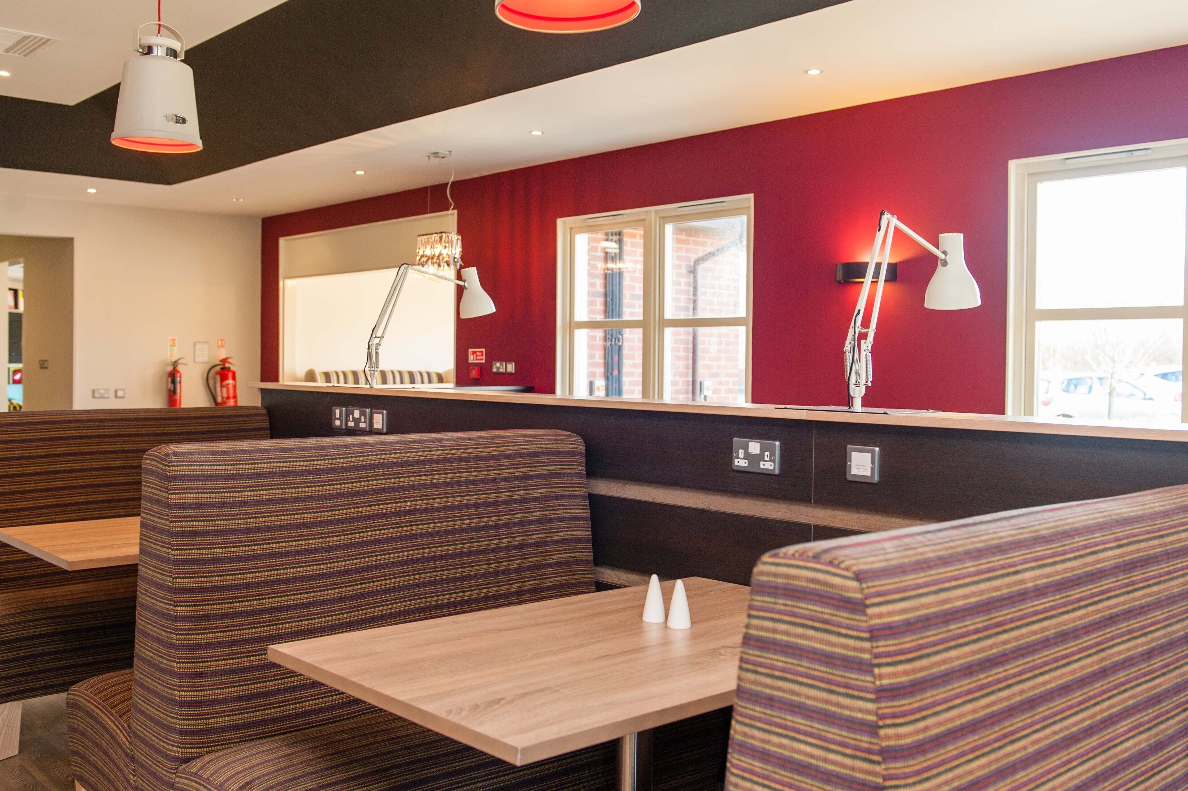 Un restaurante moderno con asientos a rayas, una mesa de madera y una pared de acento roja.