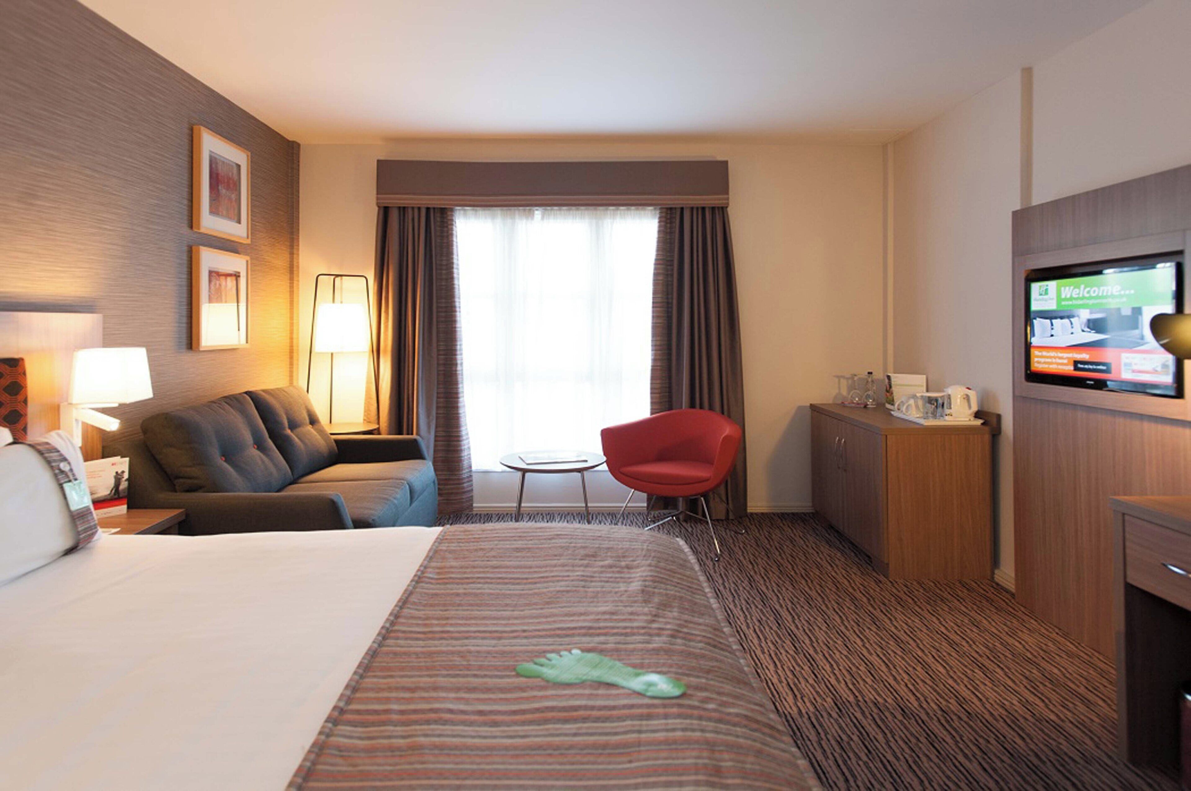 A hotel room with a bed, a desk, a chair, a TV, and a window with curtains.
