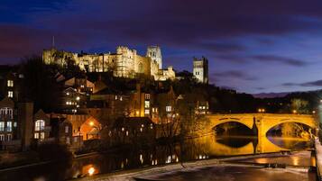 A historic castle with a bridge over a river, surrounded by buildings.