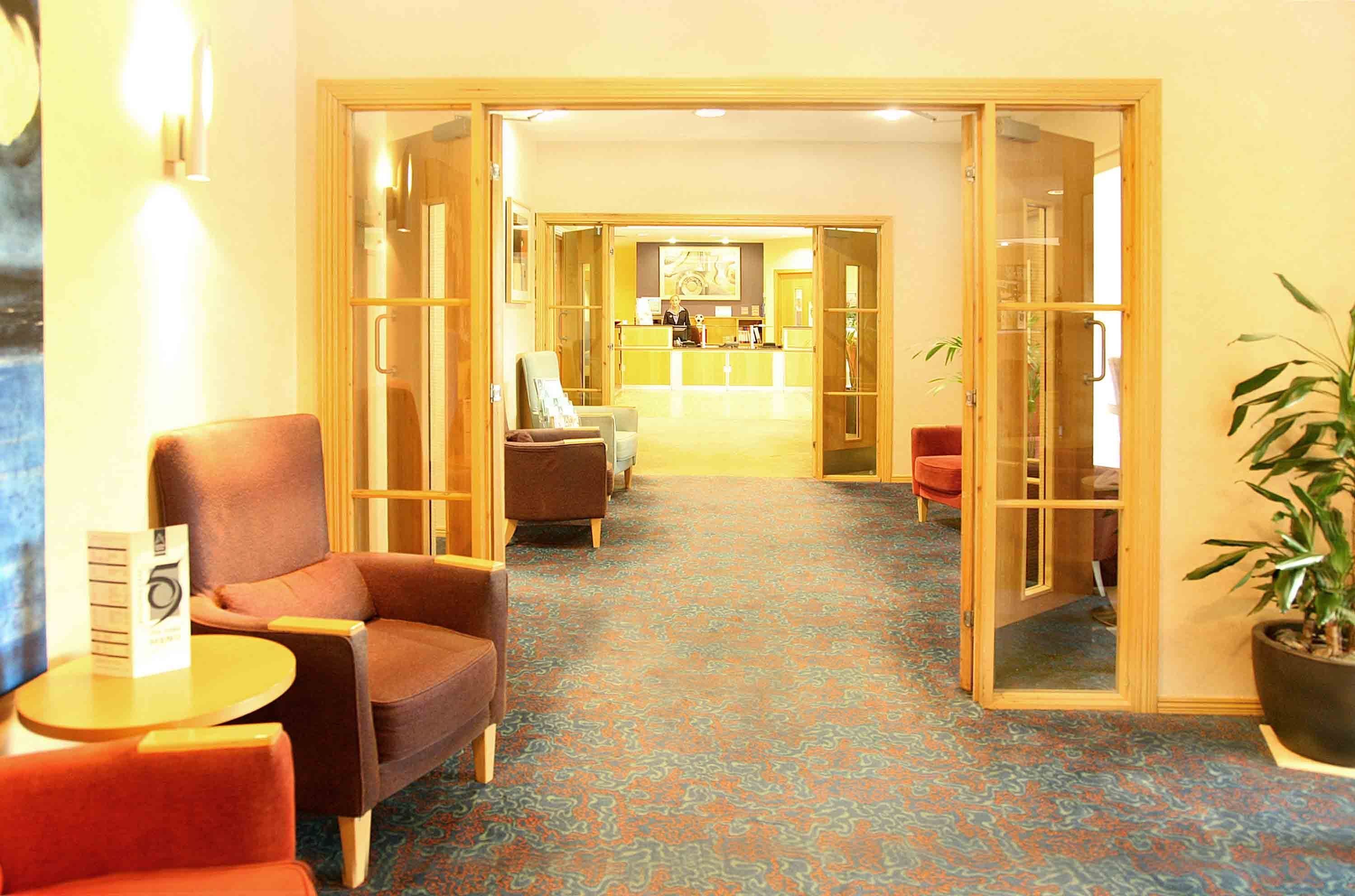 Un hall de hotel con mostrador de recepción, zona de estar y piso alfombrado.