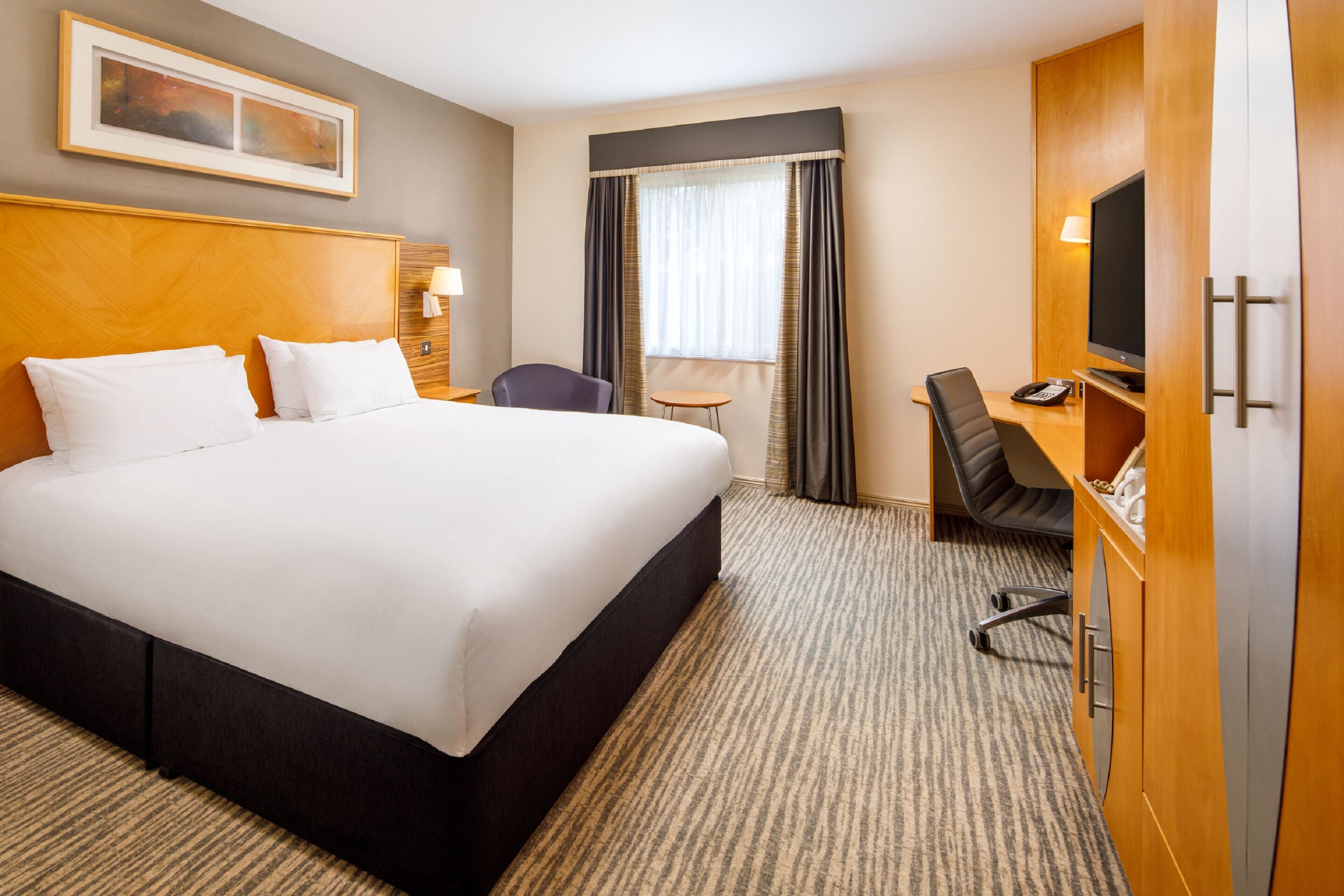 Una habitación de hotel con una cama grande, un escritorio con silla, un televisor y una mesita.