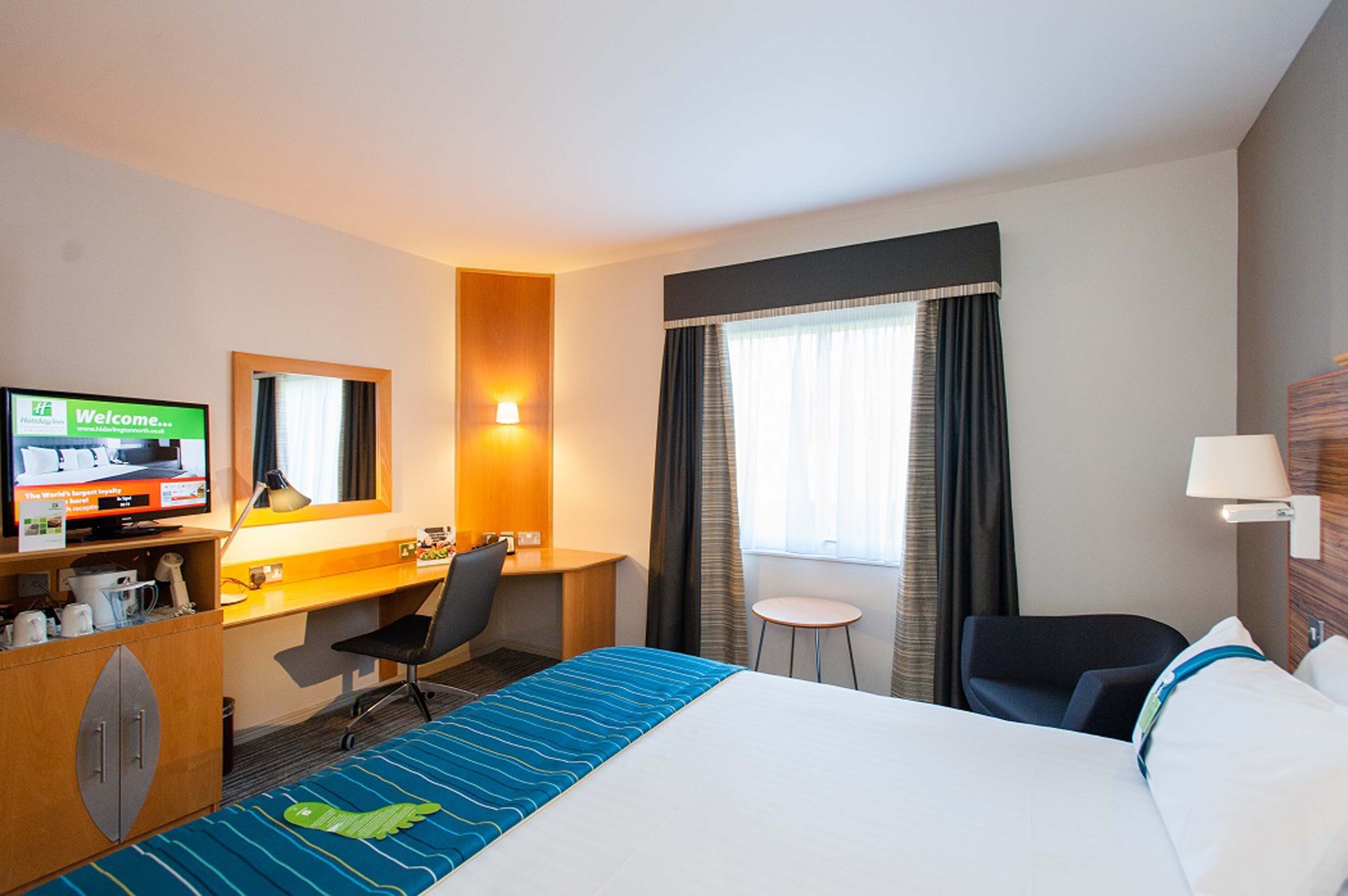 Habitación de hotel con una cama, un escritorio con computadora, televisión, una mesita y una silla.