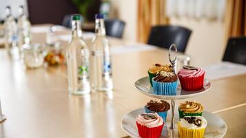 A table with a three-tiered stand holding colorful cupcakes, clear glass bottles, and a small plant.