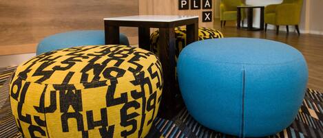 A room with a wooden wall, a blue sofa, a yellow patterned ottoman, and a small table.