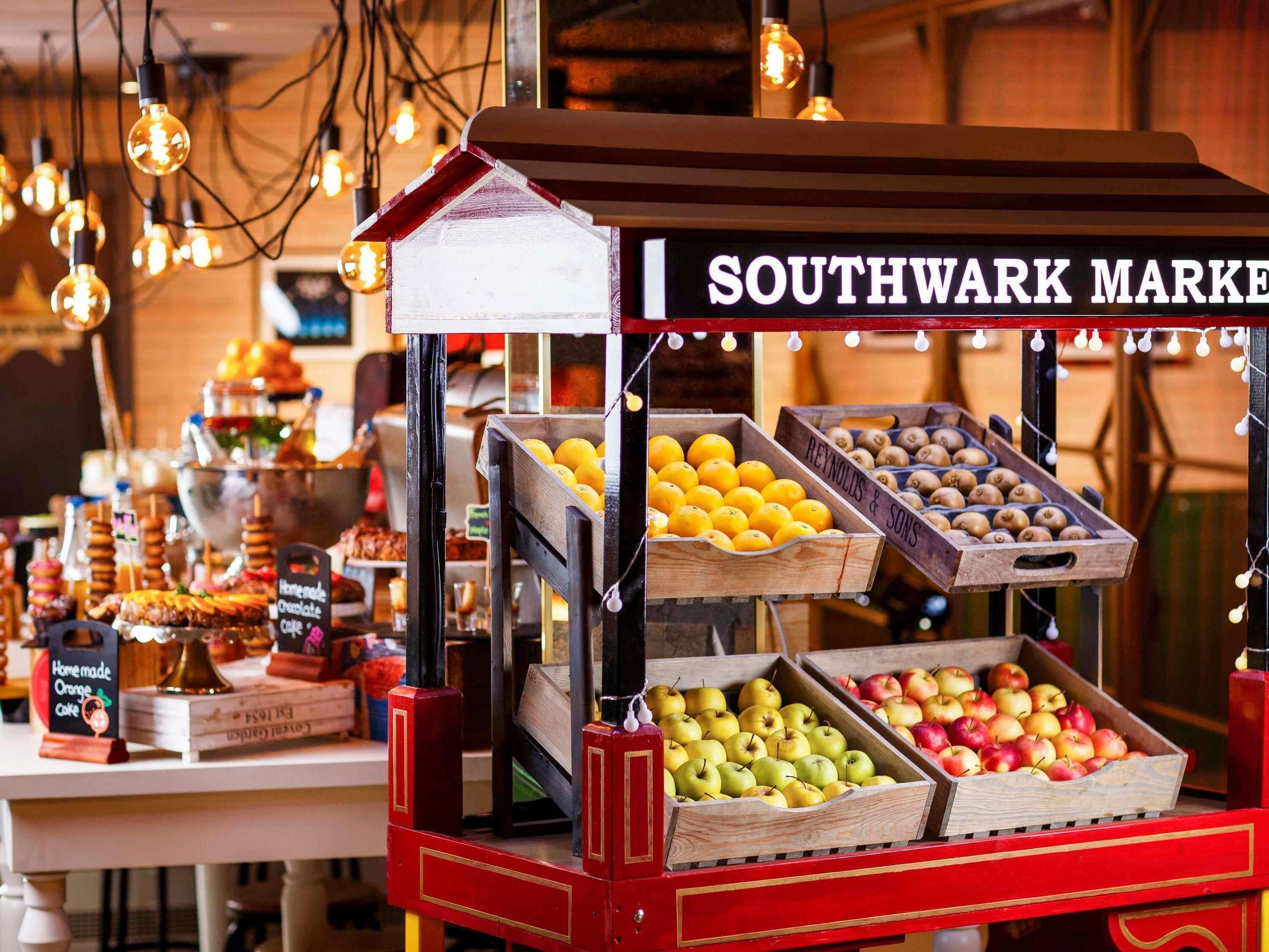 A Southwark Market stall with wooden crates of apples, oranges, and pears, and a sign reading 'Southwark Market'.