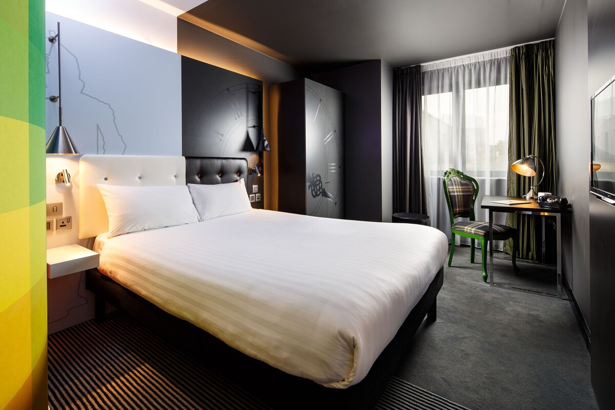 A modern hotel room with a large bed, a desk, and a chair.
