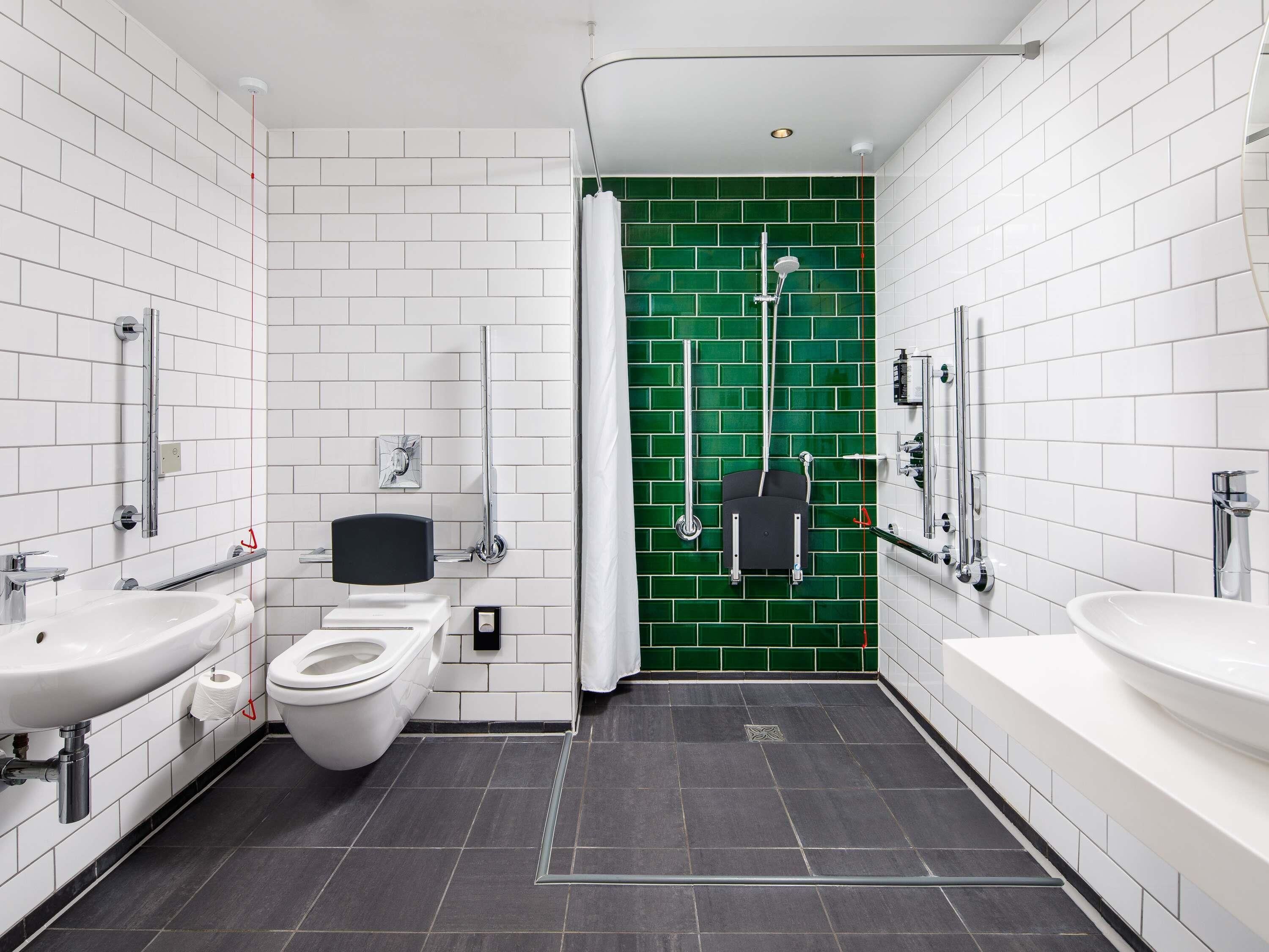 A modern bathroom with white subway tiles, a green accent wall, a white toilet, a sink, and a shower area.