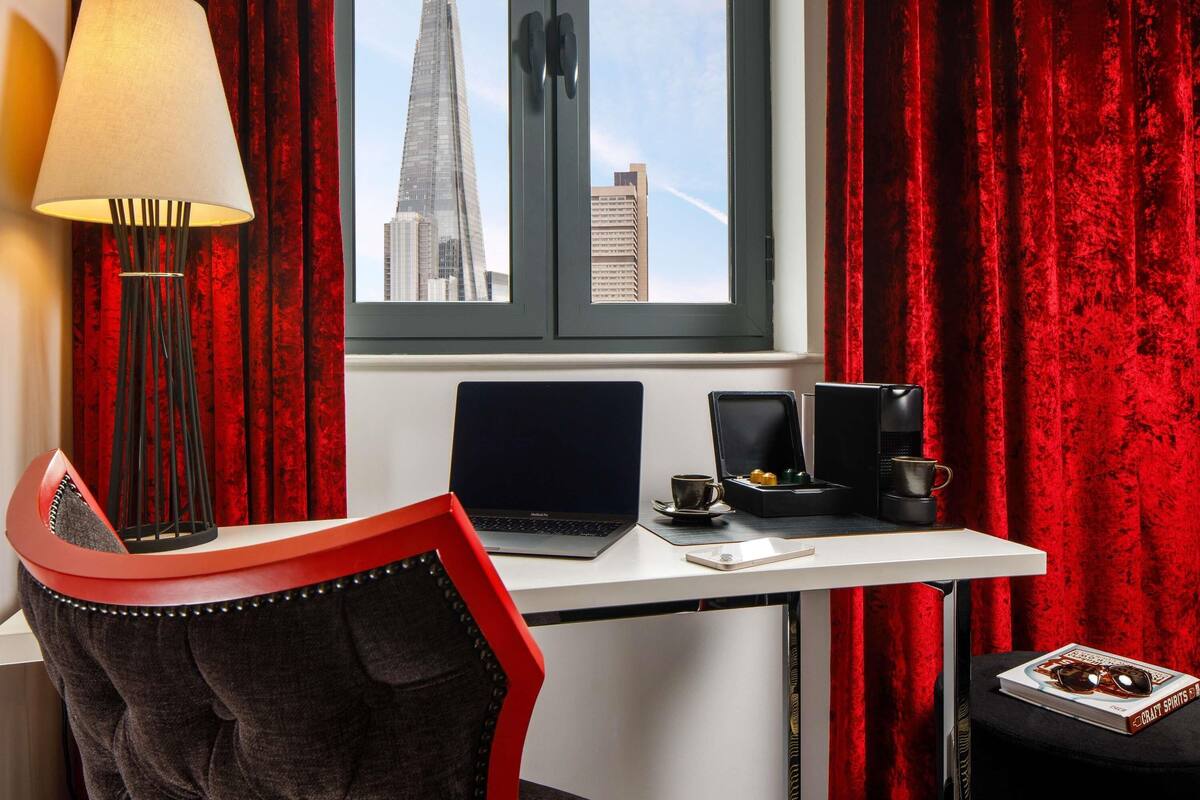 Une chambre d’hôtel moderne équipée d’un bureau, d’un ordinateur portable et offrant une vue sur un grand immeuble.