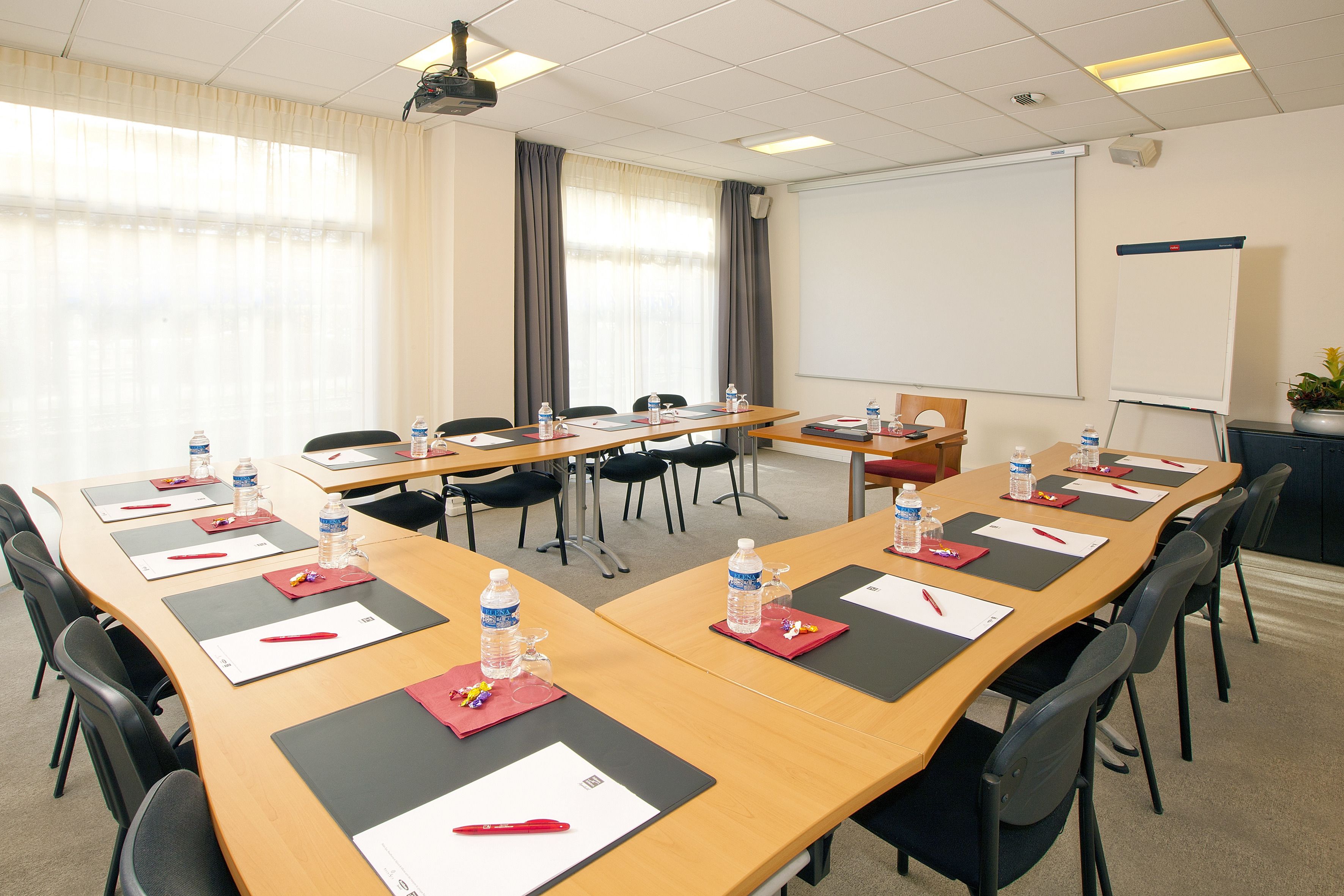 Une salle de conférence avec une longue table, des chaises, des bouteilles d’eau et des plaques nominatives.