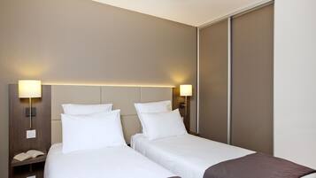 Quarto de hotel com duas camas, uma mesinha de cabeceira com abajur e uma porta de correr.