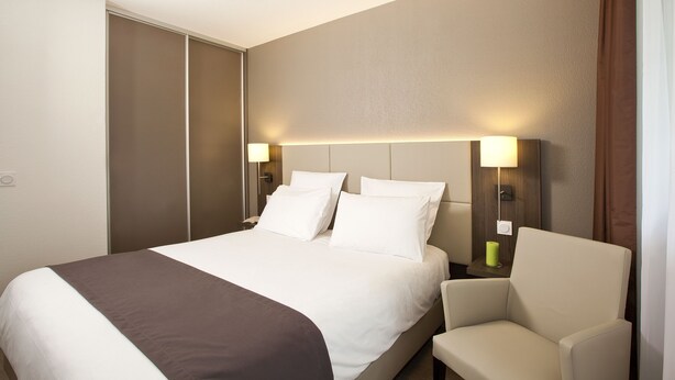 Habitació d'hotel amb un llit, dues làmpades de nit, una cadira i una taula de nit.