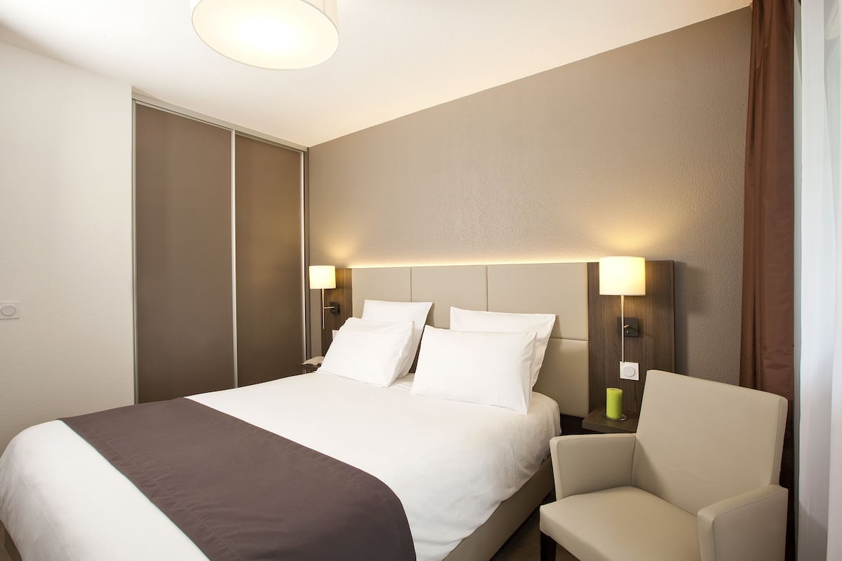 Une chambre d’hôtel avec un lit, deux lampes de chevet, une chaise et une table de chevet.