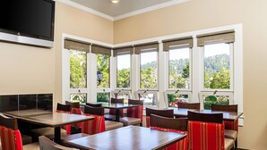 A restaurant with multiple tables and chairs, large windows with views of greenery, and a flat-screen TV mounted on the wall. - Comfort Inn Monterey Peninsula Airport (Monterey)
