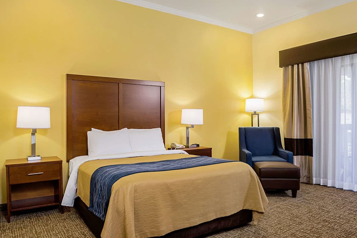 A hotel room with a large bed, two bedside tables with lamps, a chair, and a window with curtains.