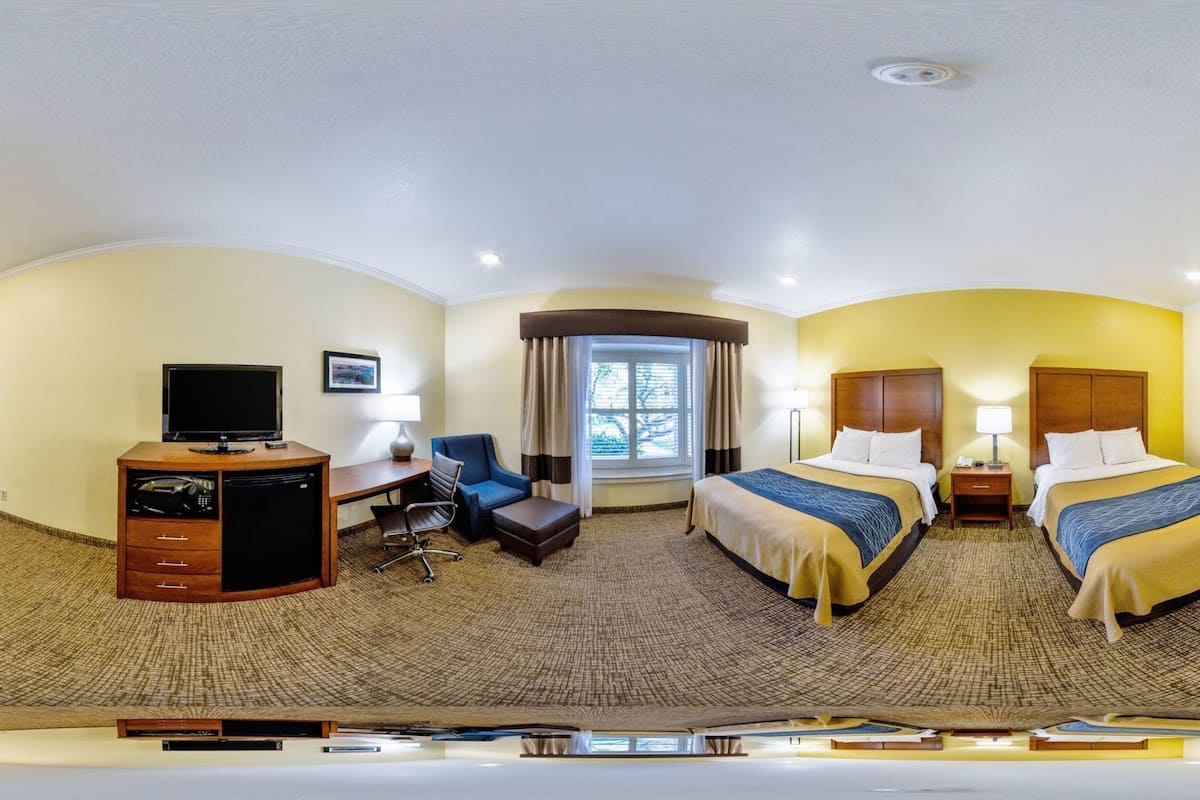 A hotel room with two beds, a desk with a computer, a chair, and a window with curtains.