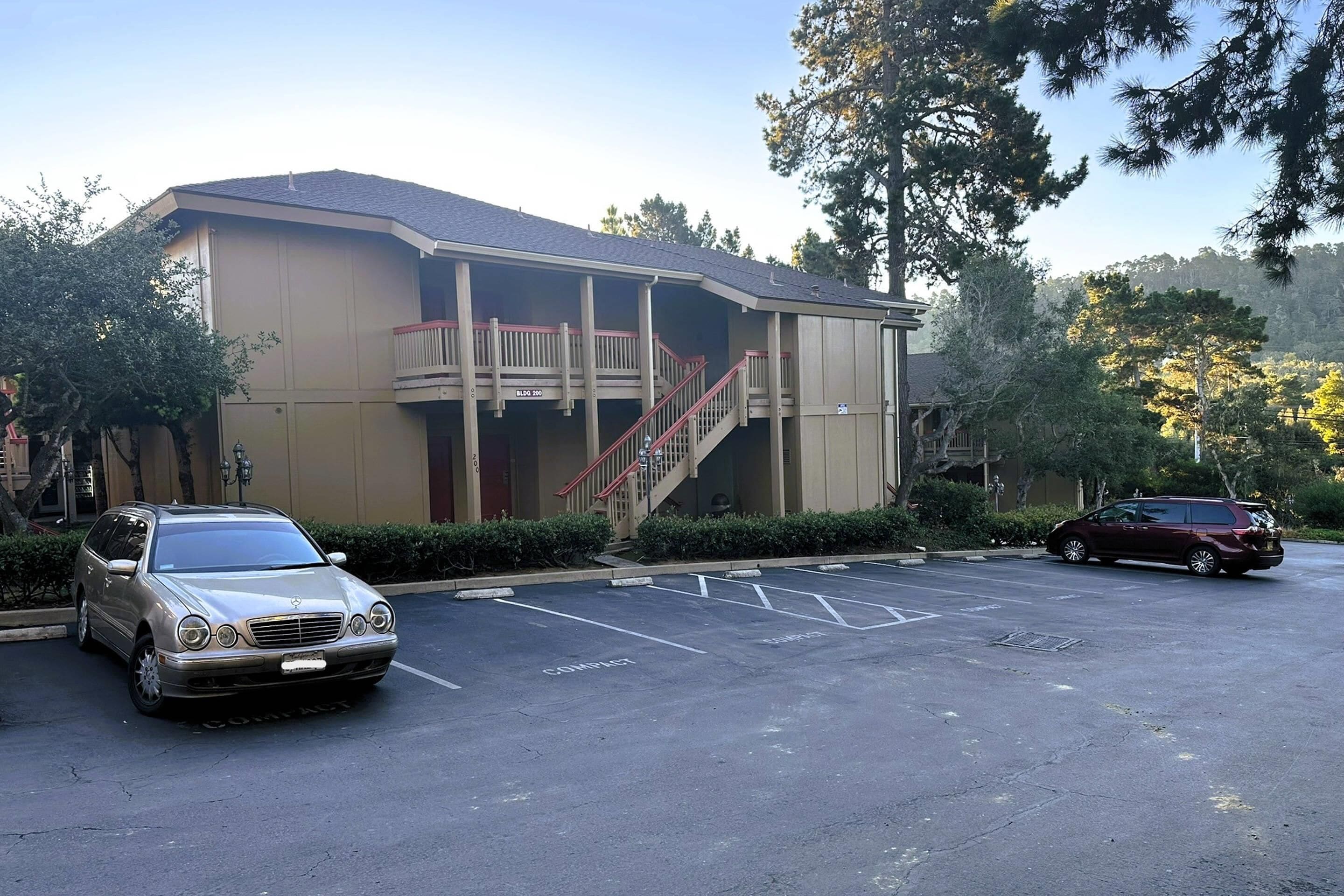 A building with a balcony and a staircase. There are two cars parked in front.
