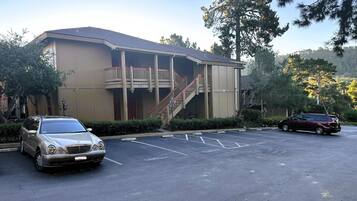 A building with a balcony and a staircase. There are two cars parked in front.