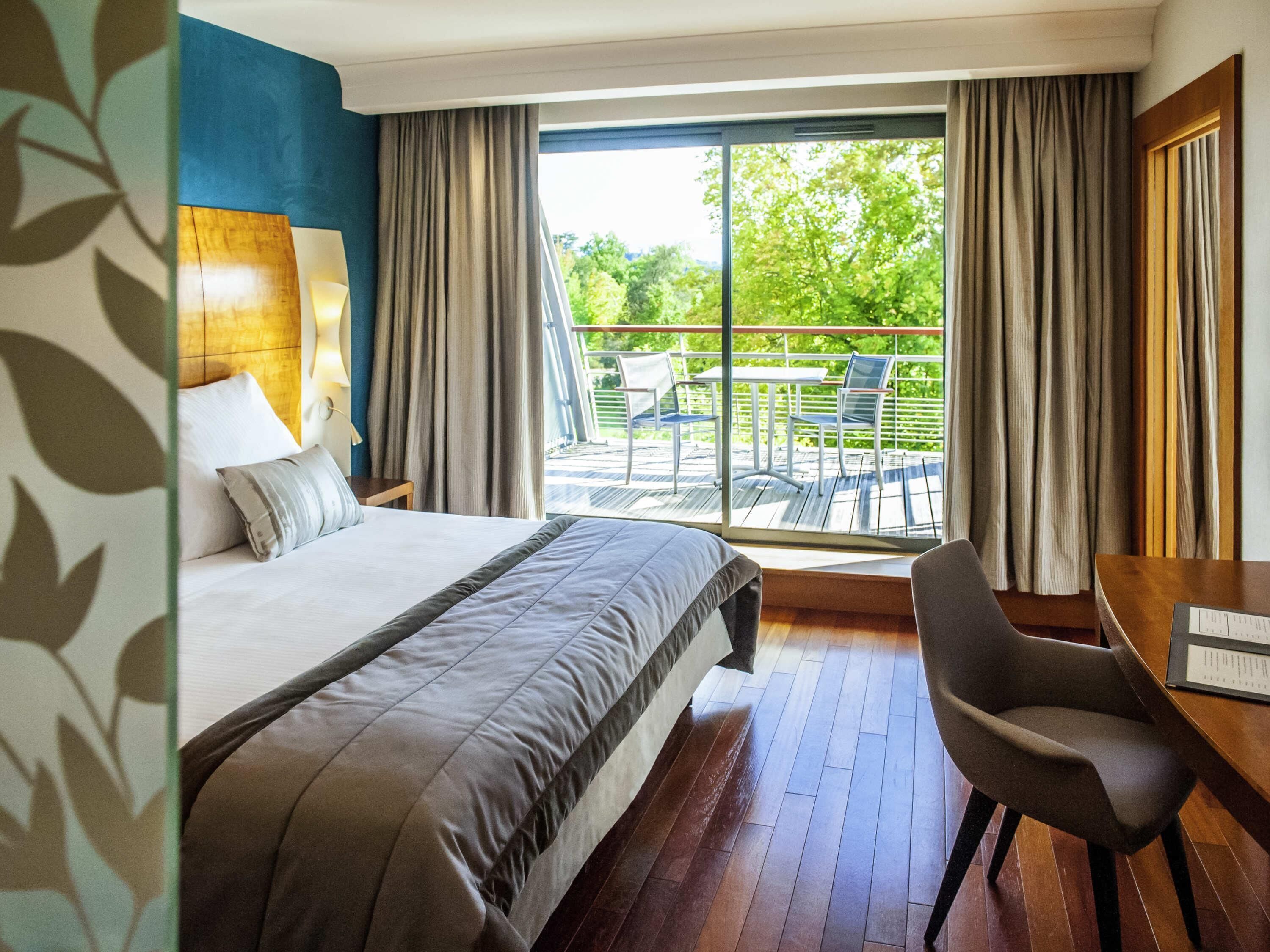 A hotel room with a bed, a desk, a chair, and a balcony with outdoor furniture.