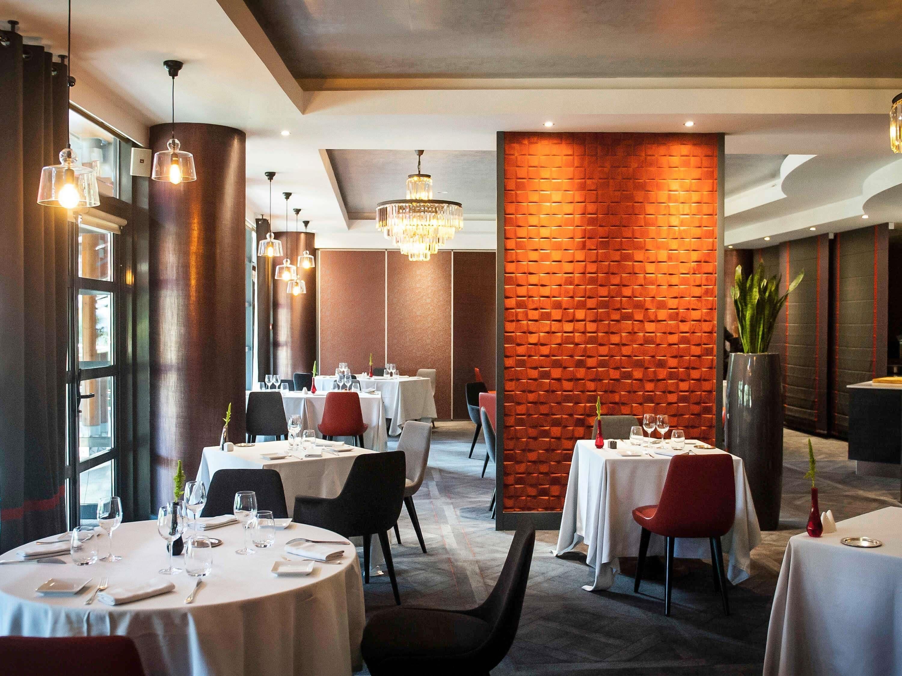 A restaurant with round tables, black chairs, and a brick accent wall.