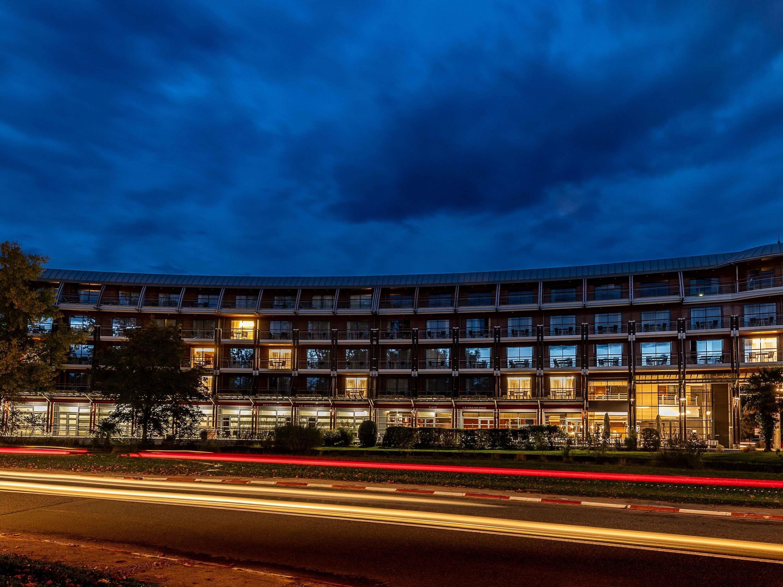 A multi-story hotel with a curved facade, multiple balconies, and a well-lit entrance.