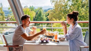 A couple dining outdoors with a table set for breakfast, including pastries, a drink, and a fruit bowl.