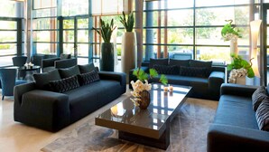 A modern living room with large windows, a sofa, a coffee table, and decorative plants.