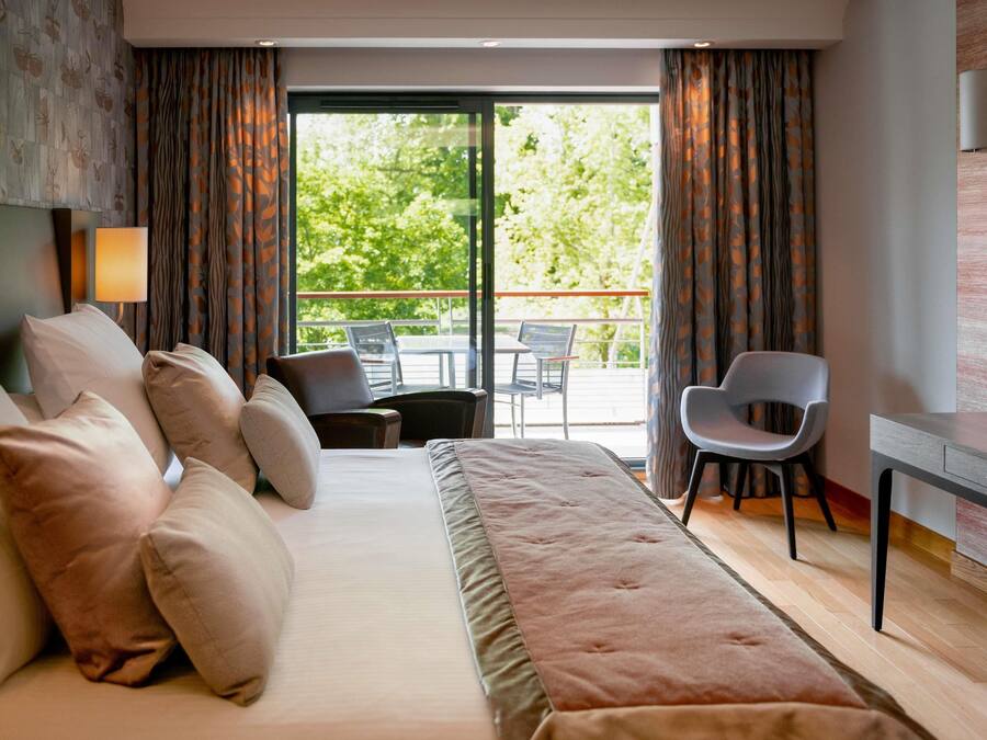 Habitación de hotel con una cama grande, un escritorio, una silla y un balcón con mobiliario exterior.