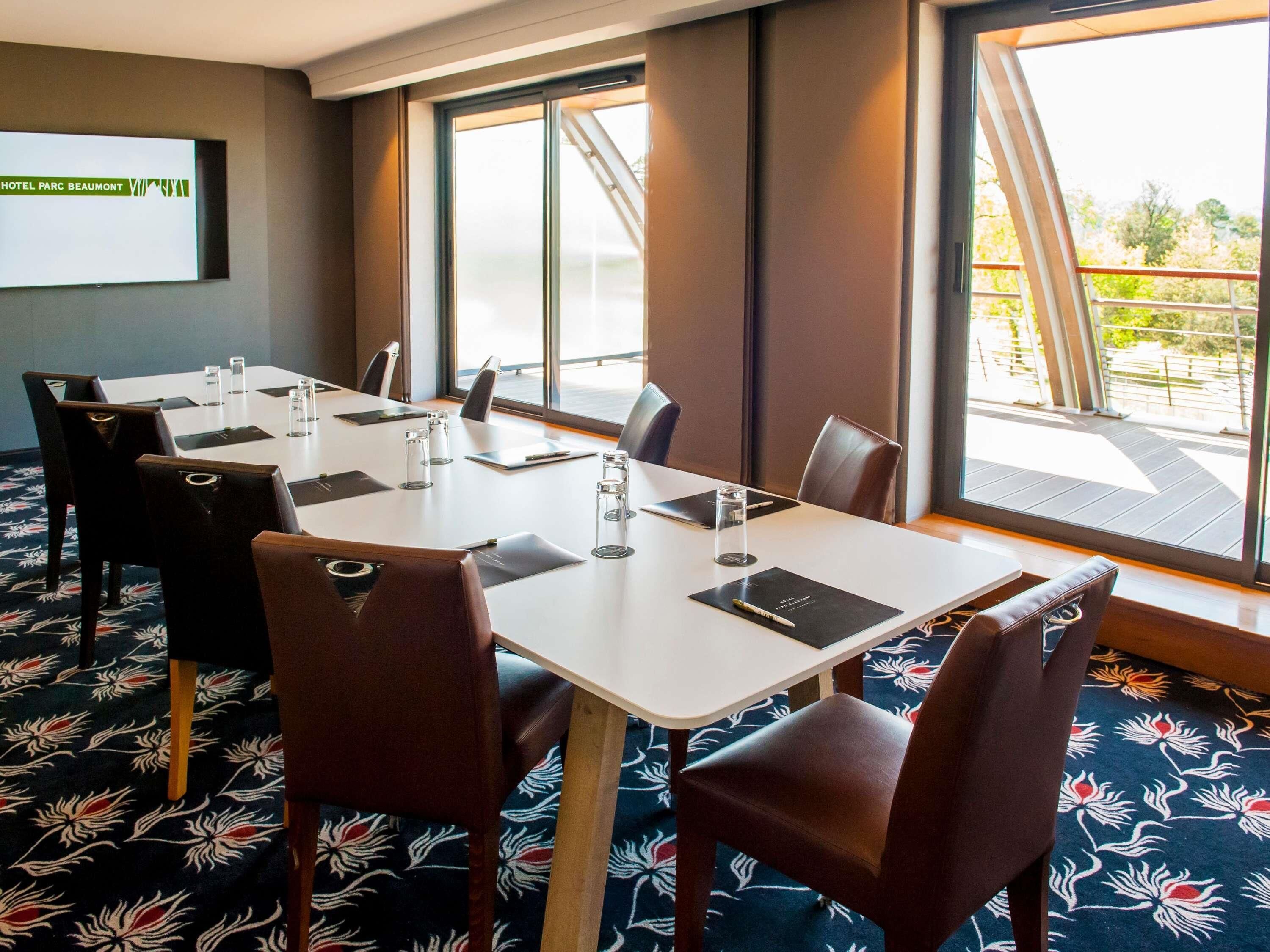 A conference room with a large table, chairs, a projector screen, and large windows with a view.