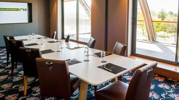 A conference room with a large table, chairs, a projector screen, and large windows with a view.