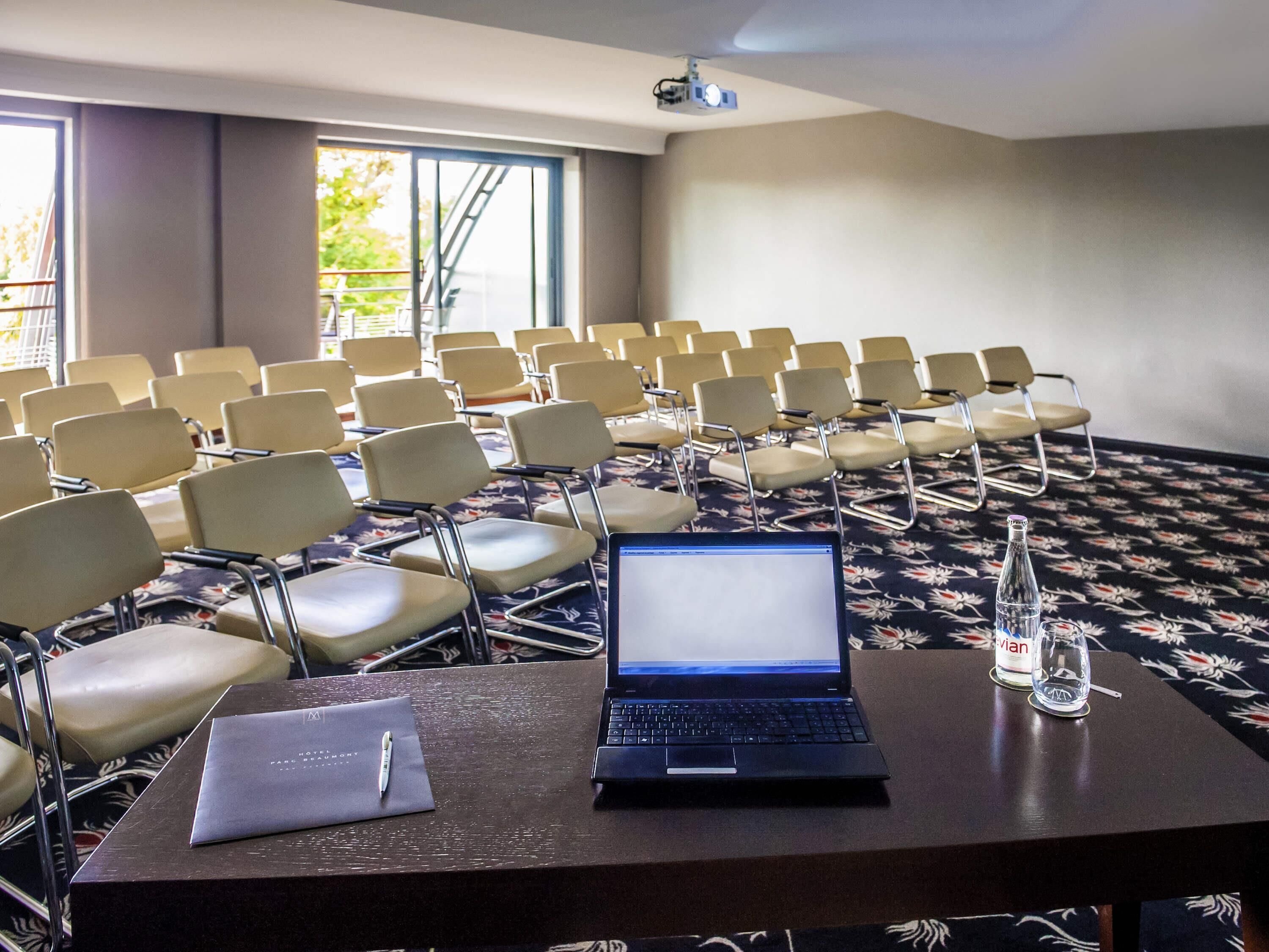 A conference room with rows of chairs, a laptop on a table, a projector, and a bottle of water.