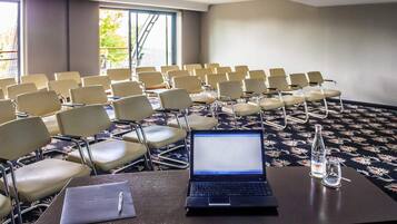 A conference room with rows of chairs, a laptop on a table, a projector, and a bottle of water.