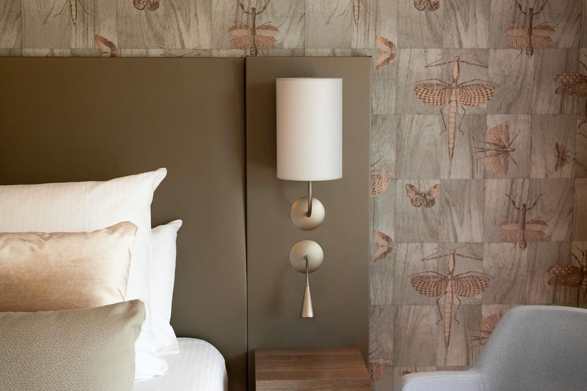 A hotel room with a bed, a bedside table, a lamp, and a chair.