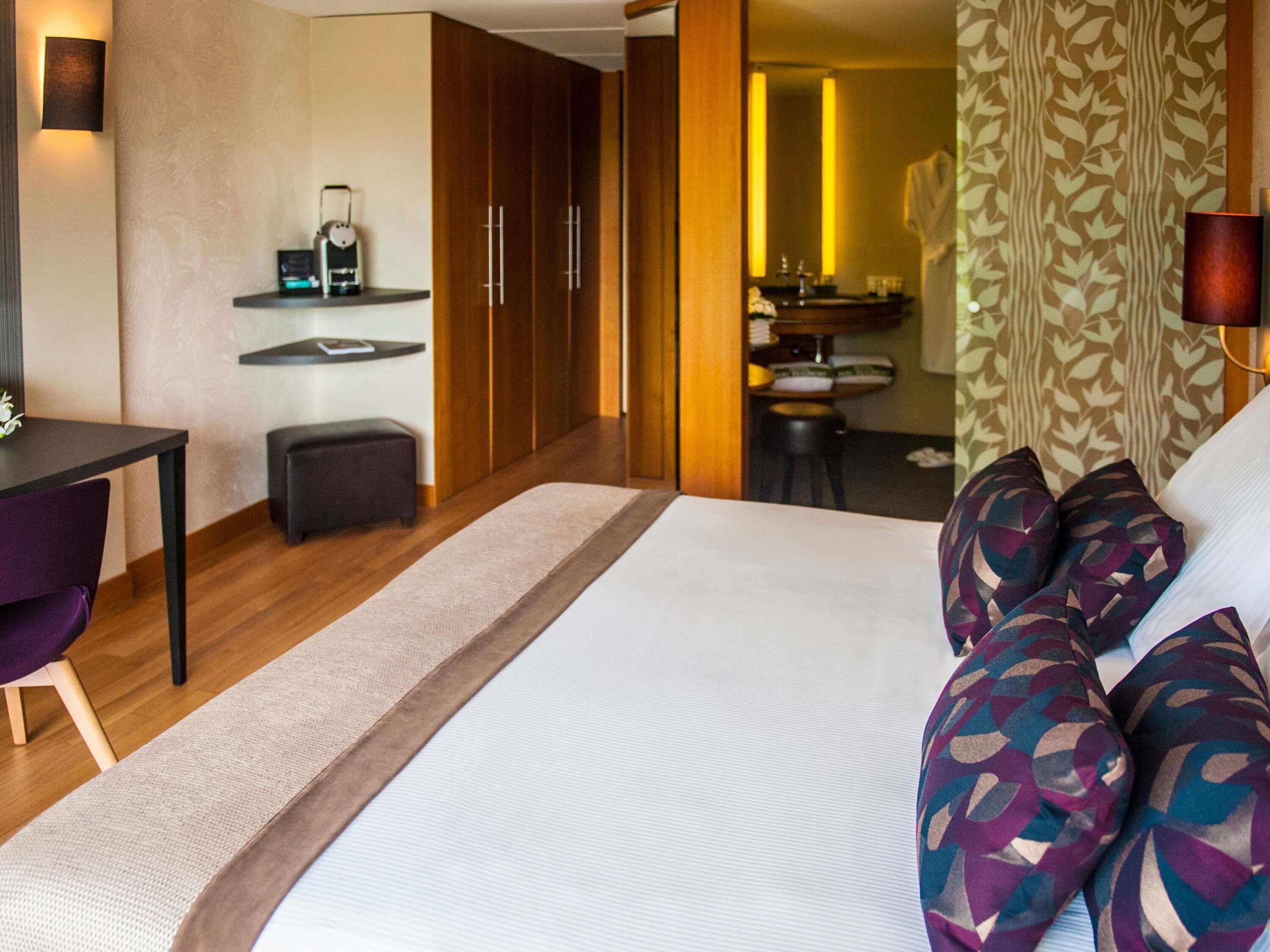 Une chambre d’hôtel avec un grand lit, un bureau, une chaise, une petite table et une armoire.