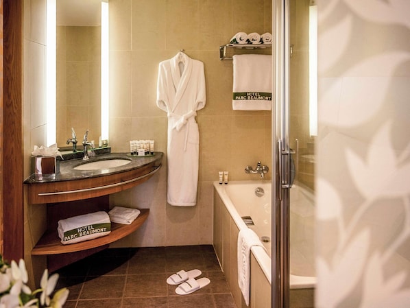 A hotel bathroom with a sink, mirror, robe, towel rack, and bathtub.