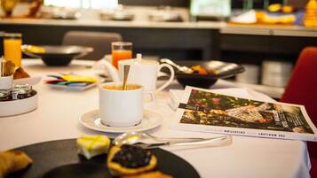 Une table de petit-déjeuner avec une tasse de café, un verre de jus d’orange, un bol de fruits et un magazine.