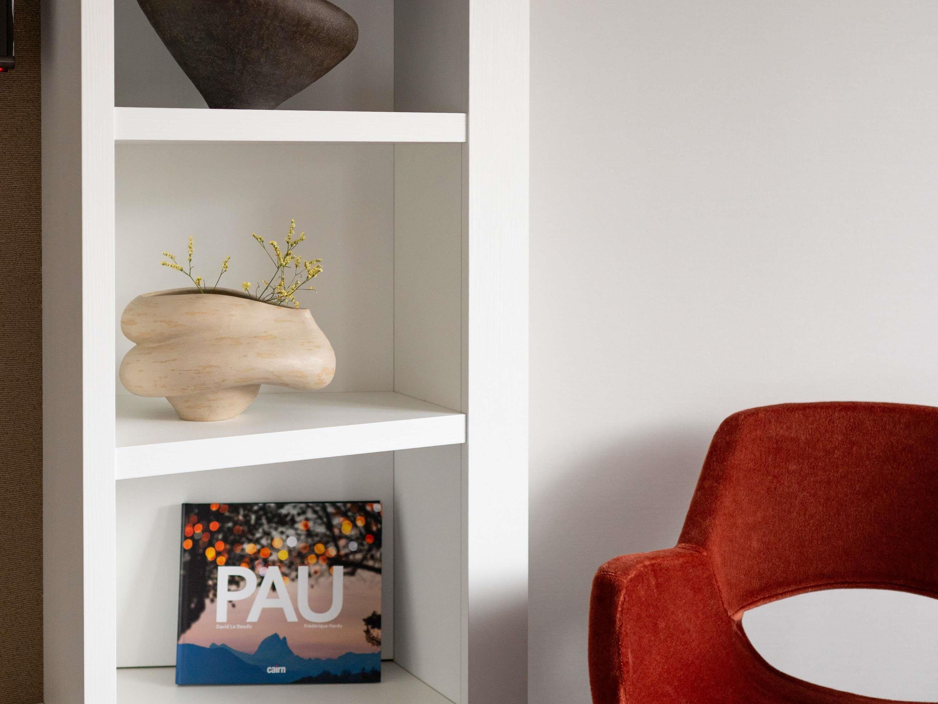 Ein Bücherregal mit einem Buch mit dem Titel 'PAU' und einer Vase mit gelben Blumen.