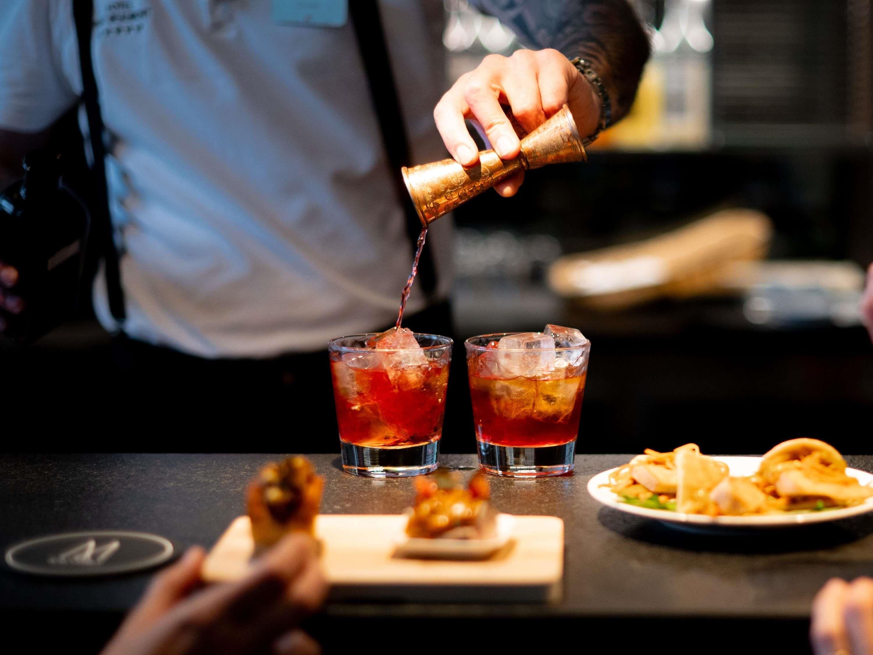 A bartender pouring a drink into two glasses with ice.
