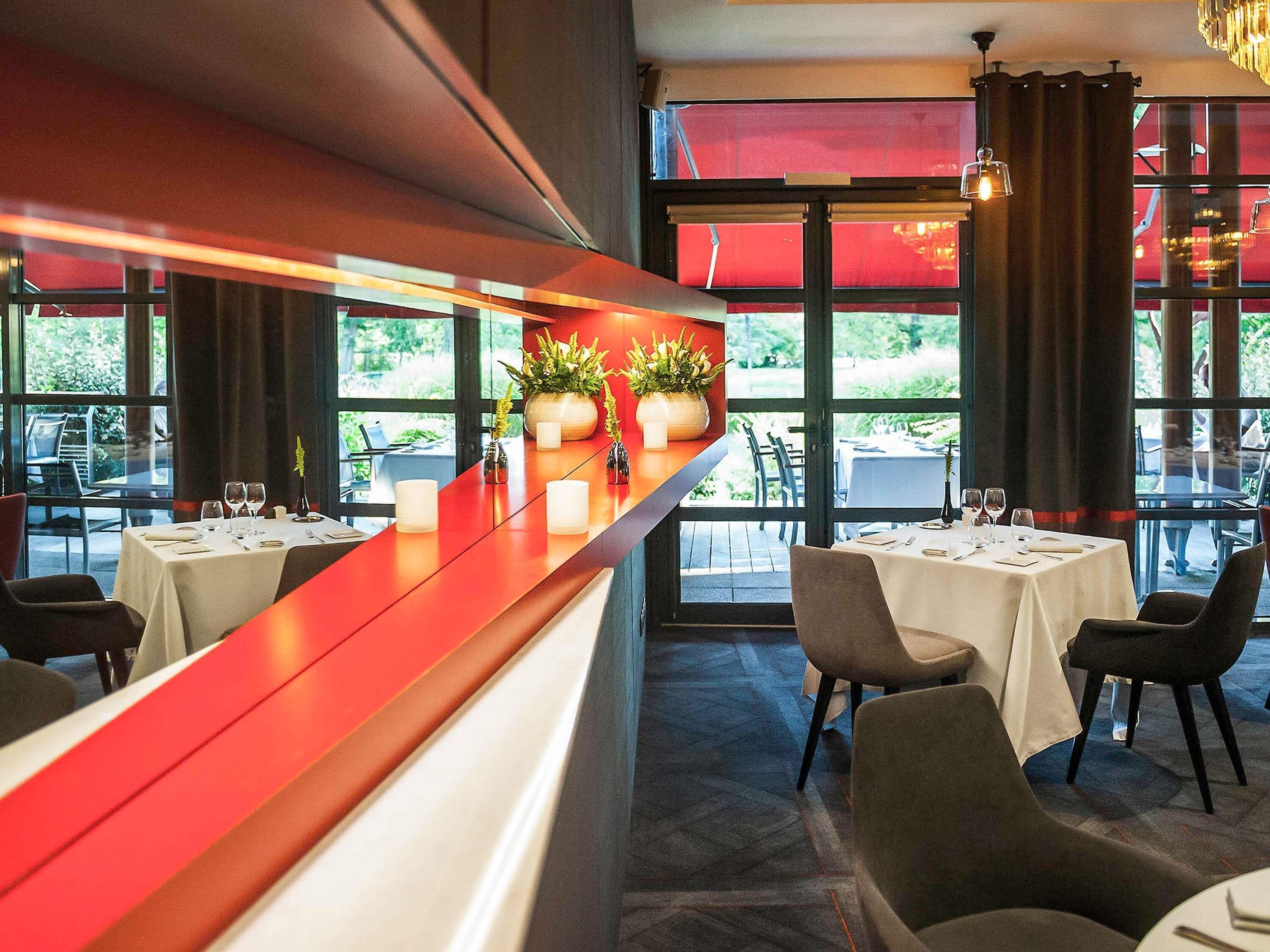 A restaurant interior with a red counter, white tablecloths, and potted plants.