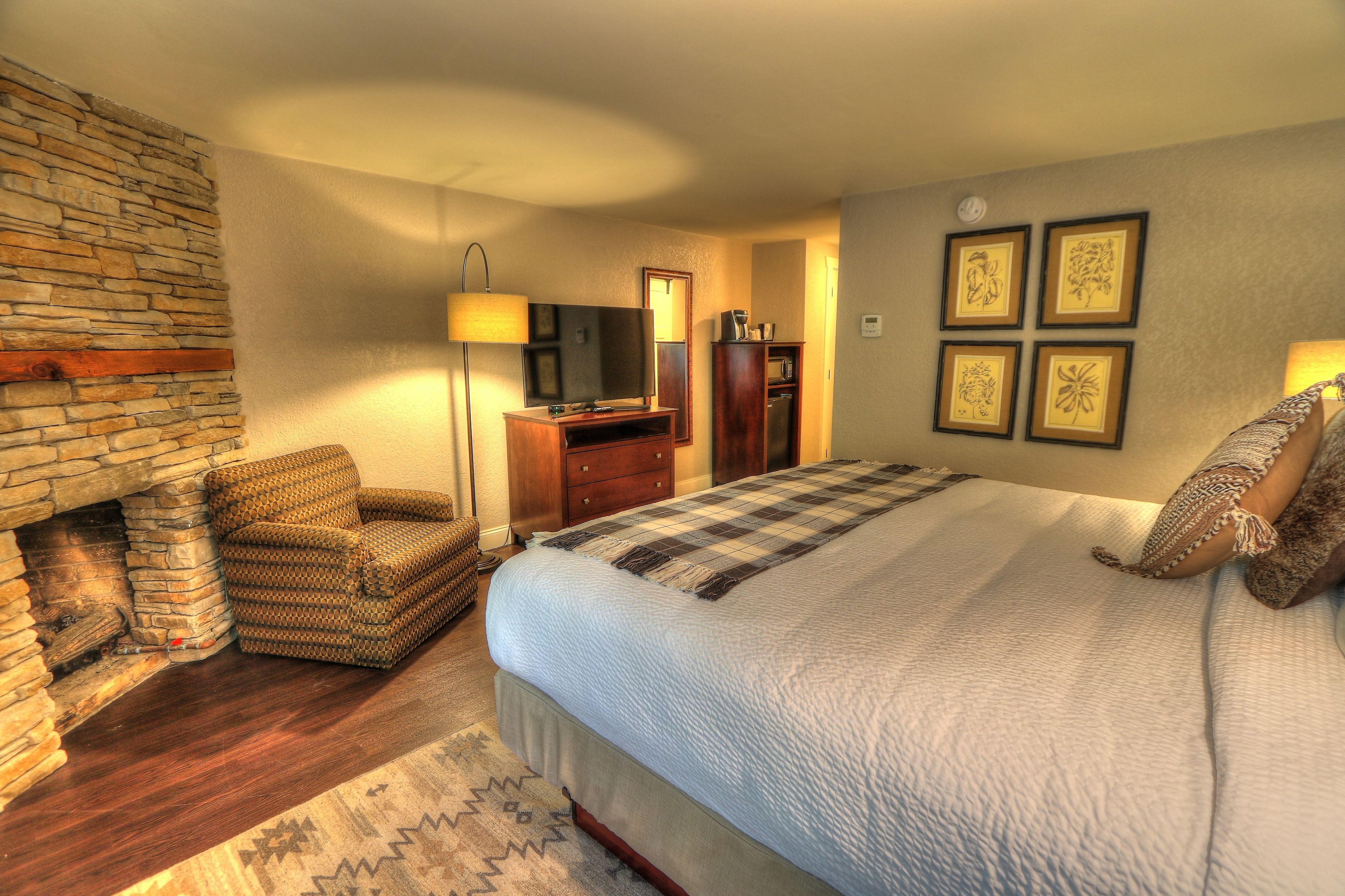 Een slaapkamer met een stenen openhaard, een groot bed met een geruite deken, een televisie, een bureau en lijstjes met kunstwerken aan de muur.