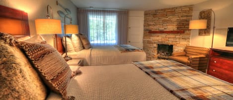Habitación de hotel con dos camas, pared de piedra, chimenea y un gran ventanal con cortinas.