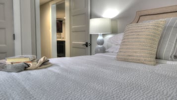 A neatly made bed with a pillow, a bedside lamp, and a book on the bed.