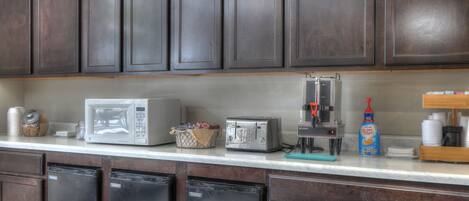 Una cocina con gabinetes de madera oscura, microondas, tostadora, cafetera y escurreplatos.