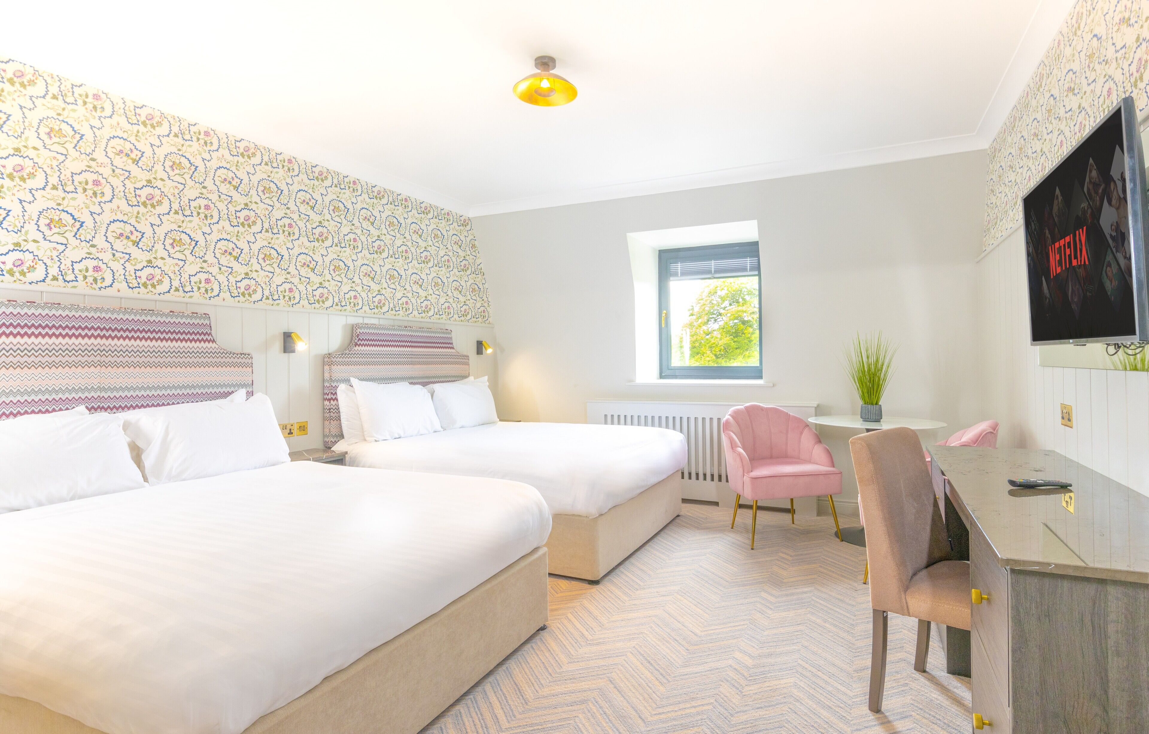 A hotel room with two beds, a desk, a chair, a TV, and a window with a view.