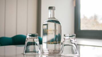 A still water bottle labeled 'BLOOMFIELD' on a table with three empty glasses.