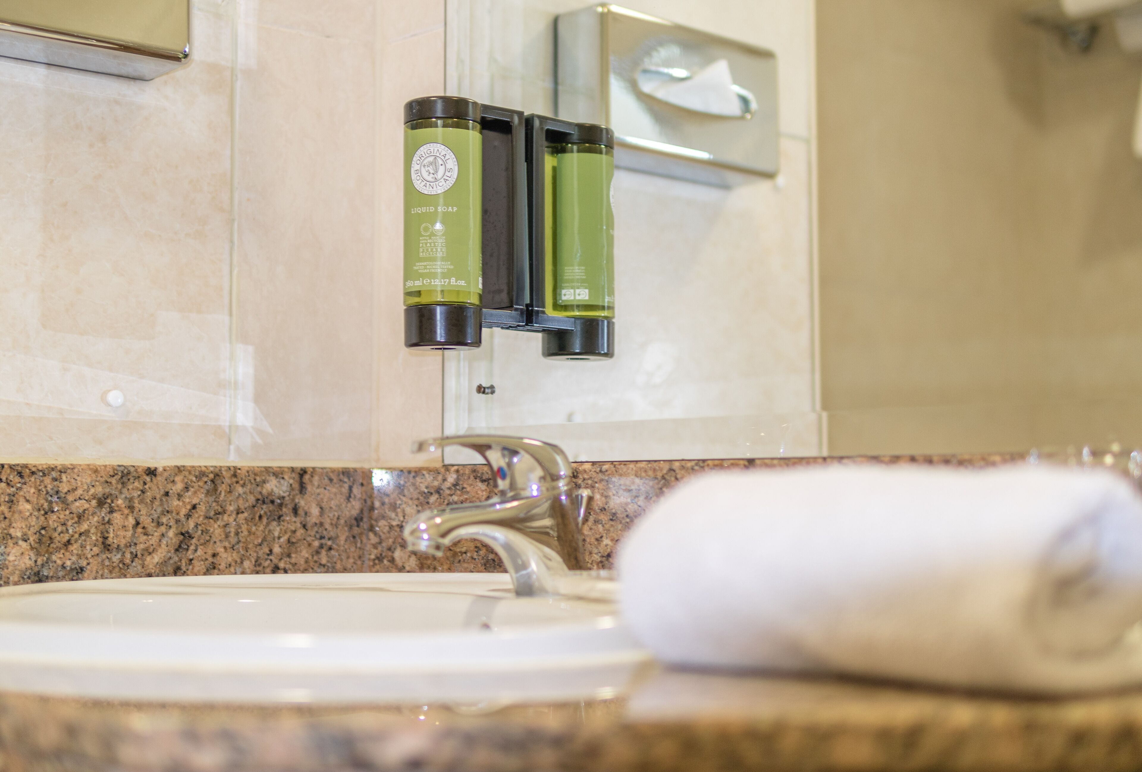 A bathroom with a sink, a mirror, and two bottles of liquid soap on a wall-mounted soap dispenser.
