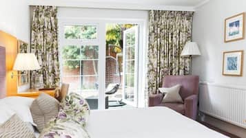 A hotel room with a bed, a chair, a table, a lamp, and a view of the outside.