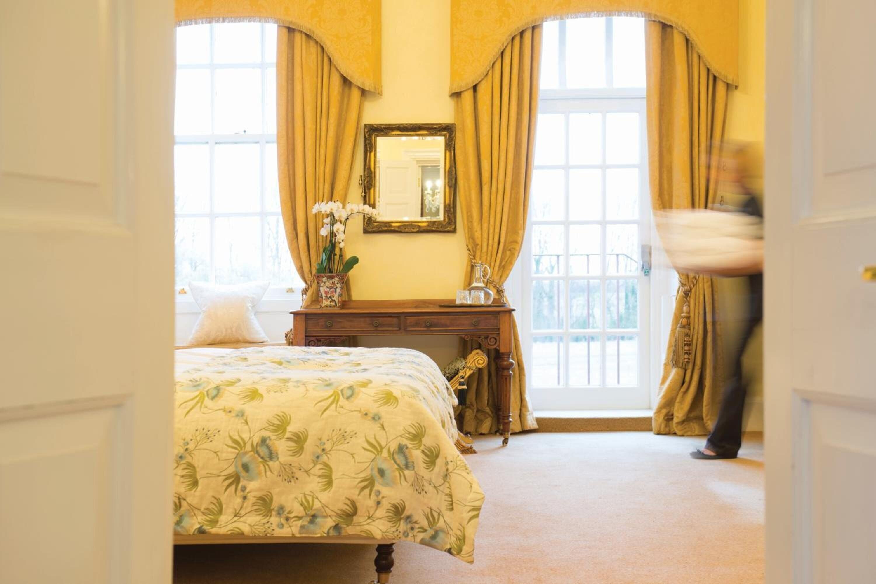 A bedroom with a bed, a dresser, a mirror, and a window with curtains.