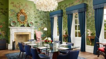 A dining room with a glass table, blue chairs, a fireplace, and a large mirror.